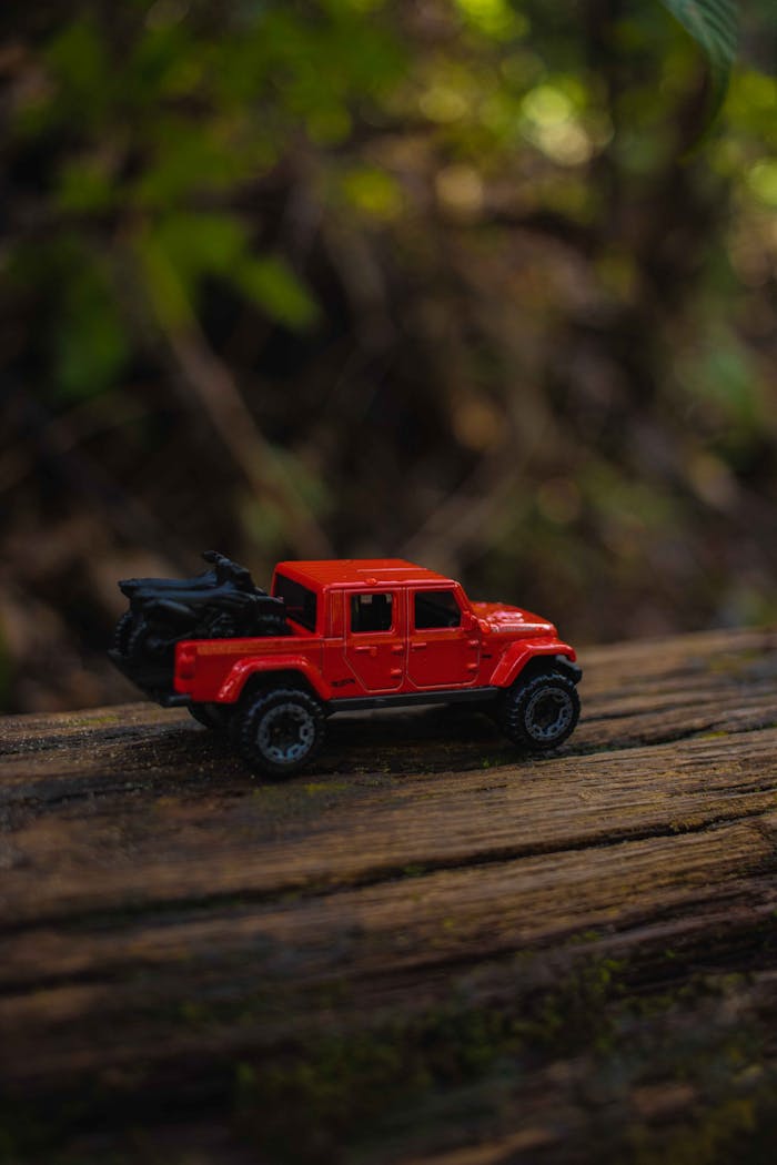 Close-up of a vintage red toy car on a rustic log in a natural setting.